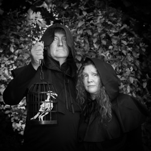 Two hooded figures holding a prop raven